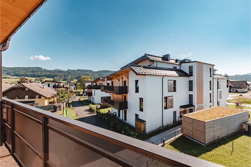 Ausblick von einem Balkon der Wohnanlage Wohnen am Sagergut auf die moderne Holzarchitektur und die umliegende Naturlandschaft in Thalgau.