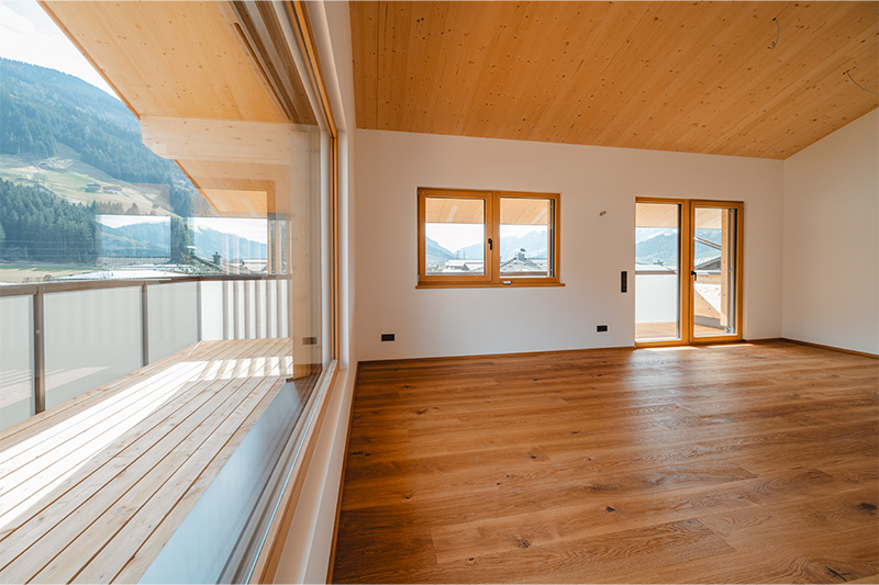 Heller Wohnraum mit Holzdecke, Parkettboden und direktem Zugang zum Balkon.