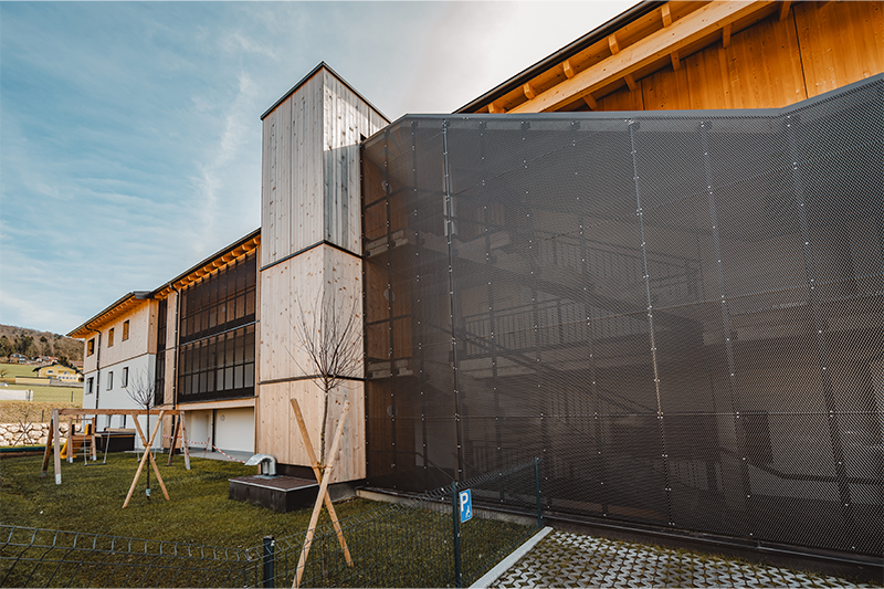 Fassadendetail der Wohnanlage mit Holzverkleidung und architektonisch gestaltetem Treppenhaus.