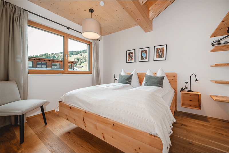 Helles Schlafzimmer im Baron Tower Saalbach mit hochwertigen Holzelementen, Doppelbett und Blick auf die Berglandschaft.