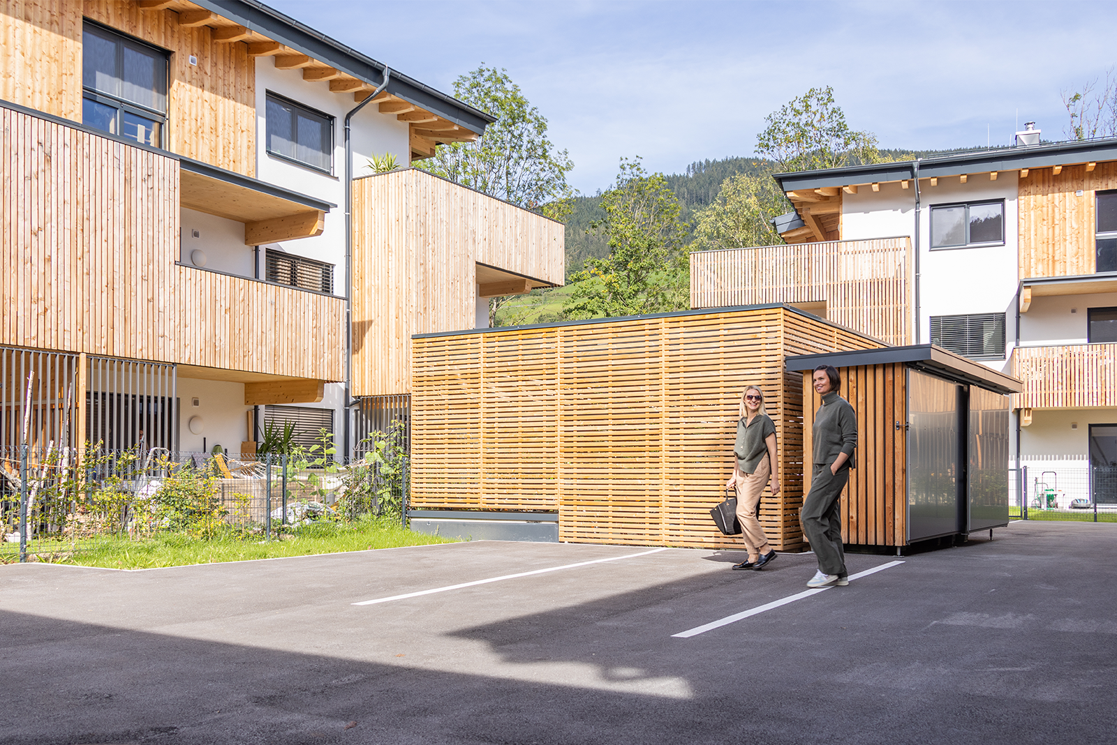 Moderne Wohnanlage in Bischofshofen mit Holzfassaden und Balkonen; zwei Personen gehen durch den Außenbereich.