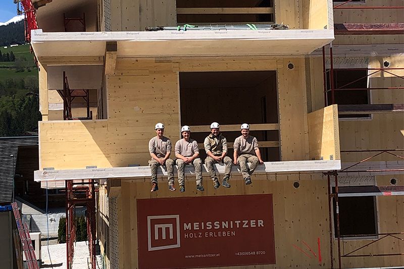 Vier Mitarbeiter von Holz Meissnitzer sitzen auf einer Baustelle eines mehrgeschossigen Holzbaus.