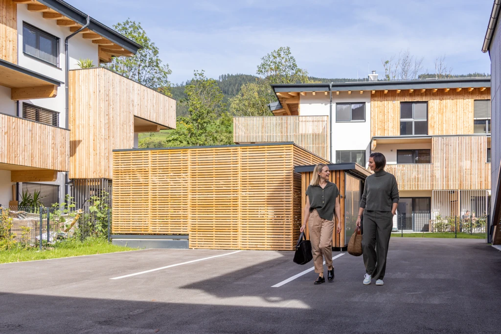Wohnbauprojekt Bischofshofen mit Holzfassaden und Balkonen, zwei Personen im Außenbereich